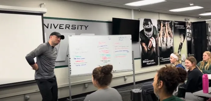 Trevor Conner talking with athletes beside a whiteboard