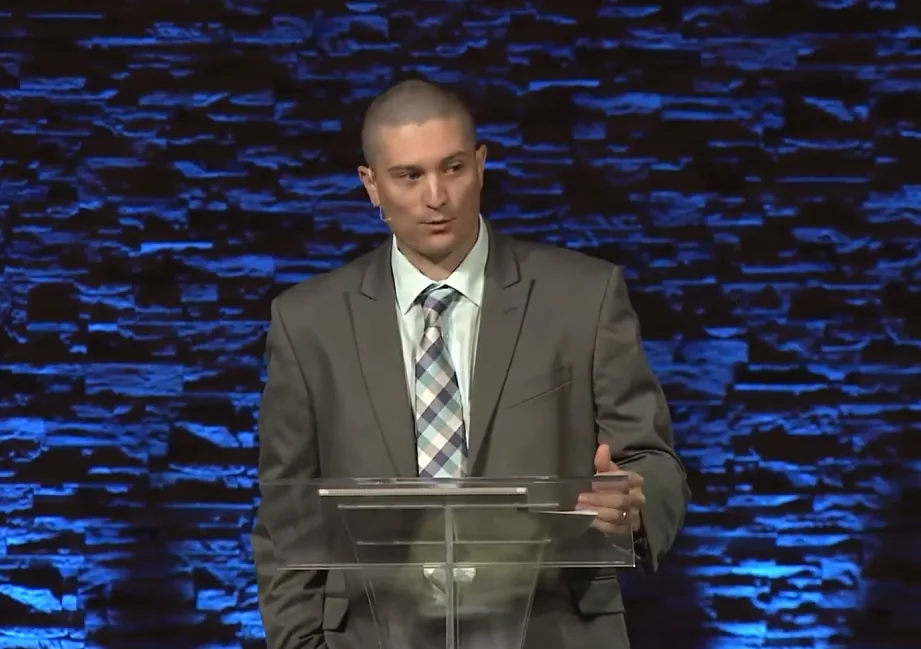 Trevor Conner speaking at a lectern in a suit
